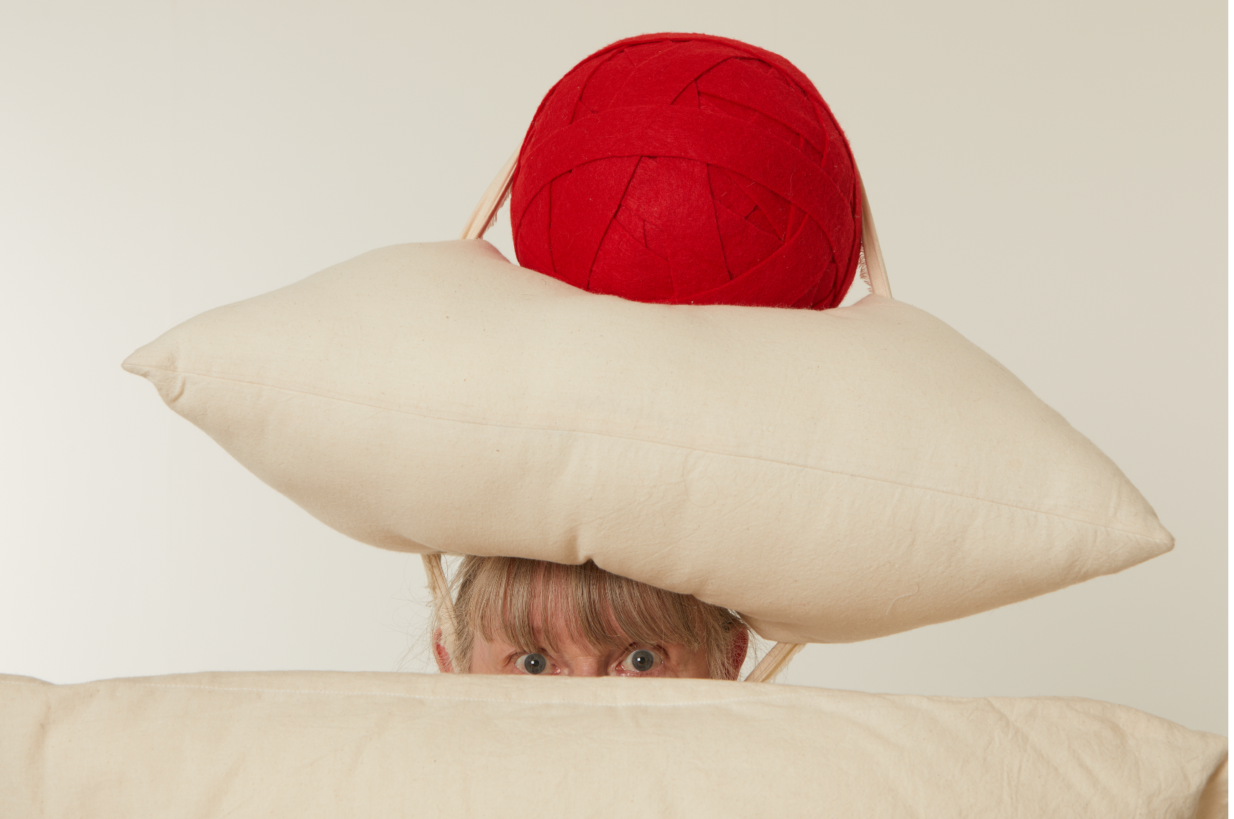 image of woman peeking out from underneath a hat shaped like a pillow with a red ball on top of the hat.